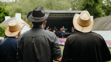 Three men standing with cowboy hats on, watching the performers on stage.