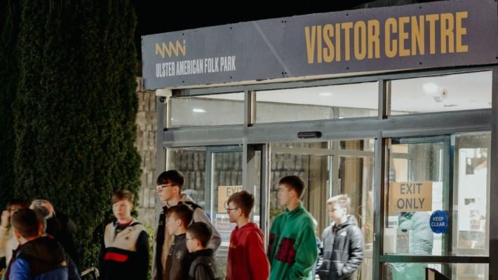 Group of kids in sweatshirts congregated outside the Visitor Centre at Ulster American Folk Park. Visitor Centre is printed in yellow on the sign above the door.