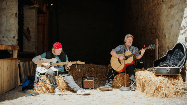 Two men playing the guitar sitting on hay bales at Bluegrass Omagh 2022